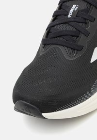 Black athletic shoe with a textured mesh upper, featuring a streamlined design, flat laces, and a white-accented midsole.