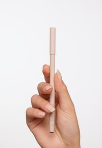 Crayon nude dans une main, en forme cylindrique, finition mate, 10 cm de long, avec une extrémité plate et un logo discret sur le côté.