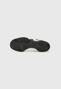 Sneaker with a black rubber outsole, textured grip patterns, and white midsole. Features a minimalist design with black accents.
