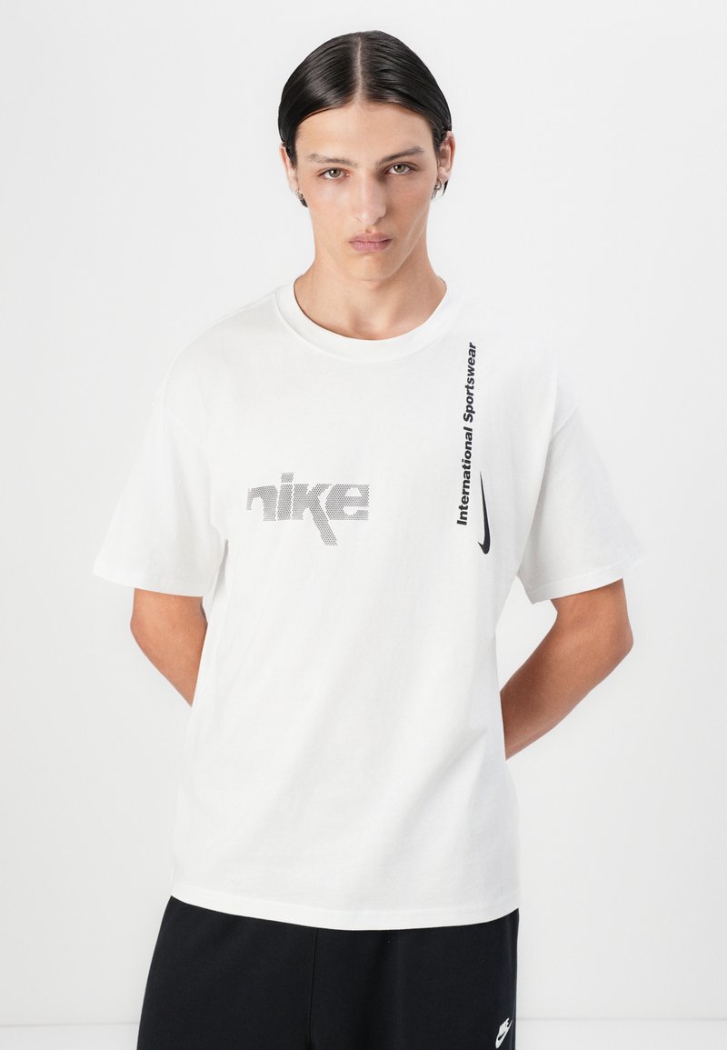 Camiseta de algodón blanca con un logo de Nike gris y texto negro que dice "International Sportswear" en vertical a lo largo del lado. Mangas cortas.