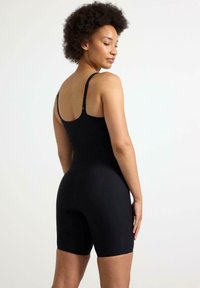 Musta bodysuit, joka on valmistettu joustavasta kankaasta, ohutolkaimilla ja tiukalla istuvuudella, jossa on lyhyet lahkeet. Sileä pintakuvio, minimaalinen koristelu.