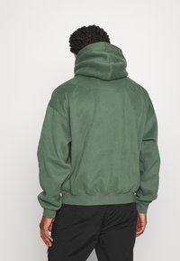 Bluza z kapturem w kolorze oliwkowej zieleni wykonana z miękkiej tkaniny; posiada duży kaptur, ściągacze na mankietach i u dołu. Prosty, luźny krój o gładkiej strukturze.