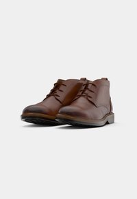 Een paar bruine leren veterschoenen tot de enkel met rubberen zolen op een witte achtergrond.