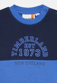 Felpa color block blu e navy con colletto a costine, caratterizzata dalla scritta "TIMBERLAND EST 1973" in lettere in grassetto e "NEW ENGLAND" sotto.