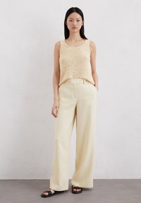 Gehaakte beige tanktop, gecombineerd met lichtgele wijde broek. Zwarte sandalen. Eenvoudig, casual ontwerp met een ontspannen pasvorm.
