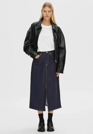 Veste en cuir noire, chemise blanche, jupe maxi en denim bleu avec fente centrale, chaussettes foncées et chaussures noires. Tenue décontractée moderne.