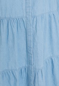 Jasnoniebieska sukienka koszulowa przypominająca dżins, z warstwowym fasonem i marszczonymi sekcjami, z guzikiem z przodu oraz miękką, textured tkaniną.