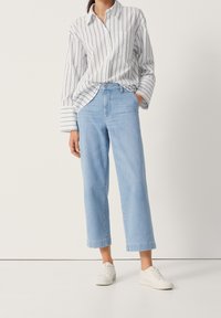 Jasnoniebieskie, szerokie dżinsy z wysokim stanem. Połączone z białą, w paski koszulą z kieszonką i podwiniętymi mankietami. Białe trampki dopełniają całość.