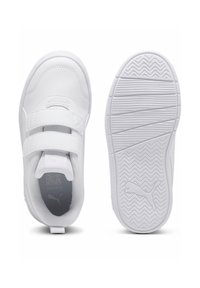 Baskets blanches avec un dessus synthétique lisse, deux bandes Velcro réglables et une semelle en caoutchouc texturée avec un motif en zigzag.