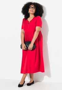 Robe rouge à manches courtes avec un zip et une taille froncée. Associée à une pochette noire et des chaussures plates. Tissu lisse et design jusqu’au genou.