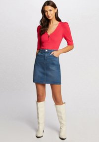 Top de rayas rojas con mangas cortas abullonadas y un botón con abertura. Falda mini de mezclilla azul con bolsillos delanteros. Botas blancas hasta la rodilla.