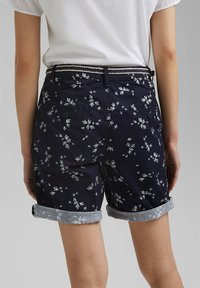 Tmavě modré šortky s bílými květinovými vzory, s ohrnutými okraji a tkaným páskem. Mají dvě zadní kapsy se zapínáním na knoflíky. Materiál: bavlna.