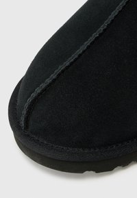 Black suede slipper with rounded toe, featuring contrast stitching along the seam and a textured rubber sole.