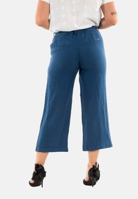 Culottes de lino azules con un diseño de pierna ancha y una cinturilla elástica, combinados con tacones negros altos con un acento de lazo.