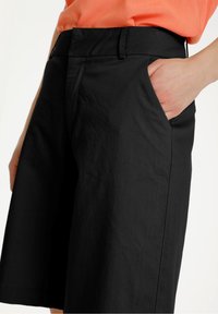 Black tailored shorts with a smooth texture, featuring side pockets and a folded waistband for adjustable fit.