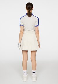 Polo grigio chiaro con accenti blu, abbinato a una gonna plissettata color crema. Calze bianche e sneakers completano l'outfit.