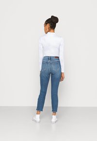 Top branco de mangas longas justo com padrão de nuvens, combinado com jeans azuis de cintura média com barra desfiada e dois bolsos traseiros. Ténis brancos.