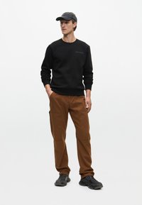 Fekete pulóver bordás mandzsettával, barna cargo nadrág több zsebbel, és fekete sportcipő. Az öltözetet egy szürke sapka díszíti.