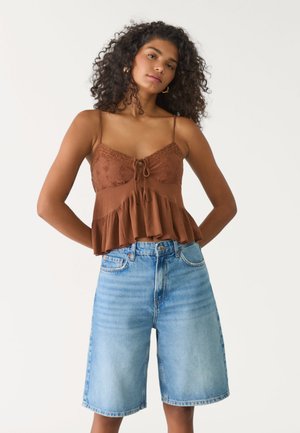 Top in marrone con spalline a spaghetti, rifinito con pizzo e orlo arricciato, abbinato a pantaloni Bermuda in denim blu chiaro con lavaggio vintage e taglio dritto.
