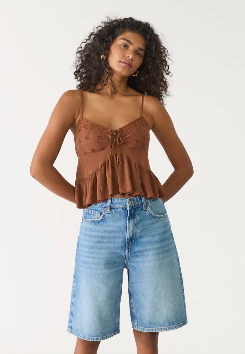 Brun spaghetti-straps topp med spetsdetaljer och en volangkant, tillsammans med ljusblå denim Bermuda-shorts med en blekt tvätt och rak skärning.