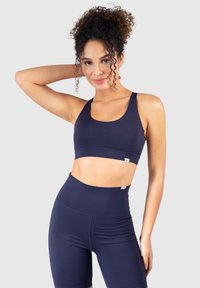 Sujetador deportivo azul marino con tirantes anchos y diseño con banda, combinado con pantalones cortos de ciclismo de talle alto en azul marino, fabricados con una tela elástica y suave.