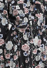 Robe en tissu noire avec un motif floral rose, blanc et bleu, fermeture à boutons sur le devant et ceinture nouée à la taille.