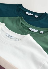 Trois t-shirts à col rond pliés en sarcelle foncée, vert et blanc, chacun avec une étiquette de marque "NEXT" et un tag de taille moyenne.