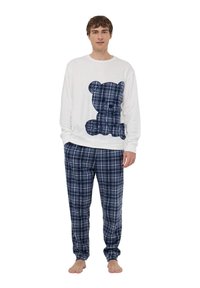 Biała koszula z długim rękawem z grafiką misia teddy w granatową kratkę; granatowe spodnie piżamowe w kratkę. Materiał wydaje się miękki i wygodny, z elastycznymi mankietami.