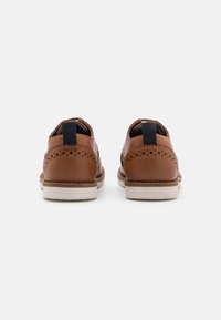 Scarpe in pelle marrone con una finitura liscia, dettagli perforati, suole in gomma crema e linguette posteriori in tessuto blu. Vista da dietro.