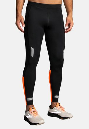 Zwarte sportleggings met oranje accenten en reflecterende details, gemaakt van rekbaar materiaal. Heeft een aansluitend ontwerp met een gladde textuur.