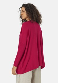 Pull fuchsia ample avec des accents côtelés, des manches longues et une silhouette décontractée. Présenté de dos. La texture semble douce.