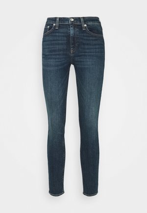 Jean skinny en denim bleu foncé avec une taille mi-haute, poches avant et fermeture à bouton. Texture lisse avec des détails de décoloration subtils.