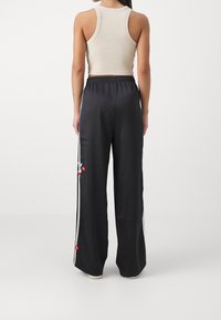 Svarta satinpants i wide-leg-modell med elastisk midja, dekorerade med vita sidostreck och röda blom- broderier.