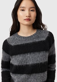 Maglione a righe nero e grigio con texture pelosa, scollo a girocollo e righe di larghezza variabile. Il materiale sembra morbido e accogliente.