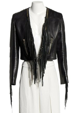 Chaqueta de cuero negra recortada con flecos largos, ojales dorados y bolsillos con cremallera, usada sobre pantalones blancos de talle alto en un maniquí.