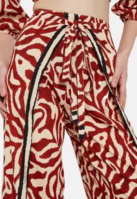 Pantalones de pierna ancha en un patrón abstracto en rojo y crema, con una cintura con cordón, acentos en negro y una tela suave y texturizada.
