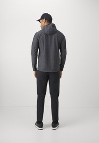 Hanorac gri închis cu glugă, asortat cu pantaloni negri și pantofi sport negri. Design minimal, textură netedă și siluetă ajustată.