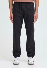 Schwarze Hose mit elastischem Bund und Knöchelbündchen, mit glatter Textur und geradem Bein, kombiniert mit weißen und grauen Sneakern.
