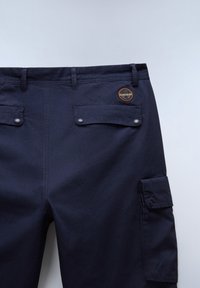 Marine cargobroek met voorzakken, knoopsluiting en logo patch. Beschikt over een gestructureerde stof en verstelbare manchetten aan de zijkant voor een op maat gemaakte pasvorm.