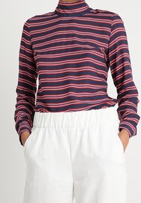 Maglia a righe blu navy e rossa a maniche lunghe con scollo alto, realizzata in tessuto morbido, abbinata a pantaloni bianchi con vita elasticizzata.