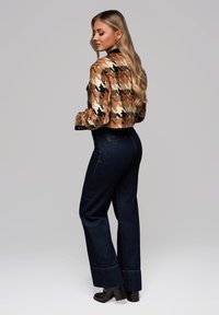 Afskåret, multicolor ternet jakke i brune og sorte nuancer parret med høj talje mørkeblå denim flared bukser og sorte hælede støvler.