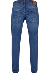 Jean en denim bleu vu de dos avec deux poches arrière, une ceinture à passants et une étiquette de marque en cuir marron sur le côté droit.