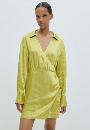 Satin Wickelkleid in leuchtendem Gelb-Grün mit tiefem V-Ausschnitt, langen Ärmeln und geraffter Taille für eine strukturierte Passform. Glatte Textur, minimalistisches Design.