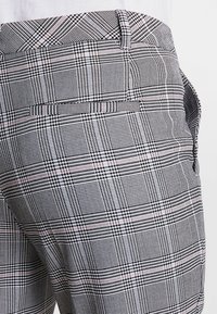 Pantalon à carreaux gris et blanc avec une coupe ajustée, des accents rose subtils, et des poches standard. Confectionné en tissu texturé.