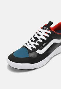Sapatilhas pretas e azuis com um cabedal texturizado, atacadores brancos e pormenores vermelhos. Apresenta um logótipo branco da Vans e uma sola de borracha durável.