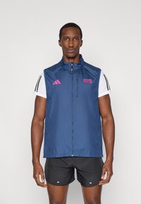 Navy sleeveless athletic vest with a zip, features pink branding and three black stripes on the shoulders, made of lightweight material.