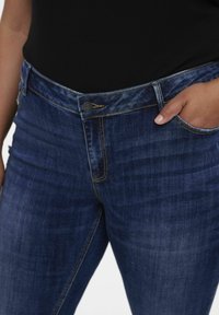 Tumedat sinised denim püksid klassikalise lõikega, millel on keskmise kõrgusega vöökoht, viis taskut ning diskreetne kuldne õmblusdetail.