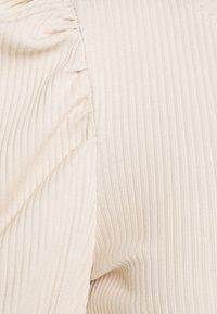 Tissu beige côtelé avec une couture froncée. Texture douce avec un léger éclat, mettant en valeur la fluidité du drapé du matériau.