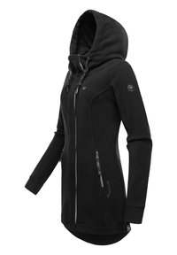 Melna vilnas jaka ar augstu apkakli un cepuri, ar rāvējslēdzēja kabatām un teksturētu audumu. Tai ir nedaudz pagarināts aizmugures dizains.