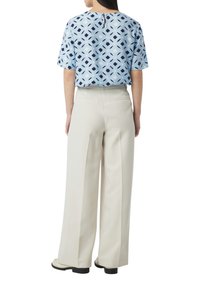 Lichtblauwe blouse met korte mouwen en geometrische patronen, gecombineerd met crèmekleurige wijde broek en zwarte schoenen. Achteraanzicht.